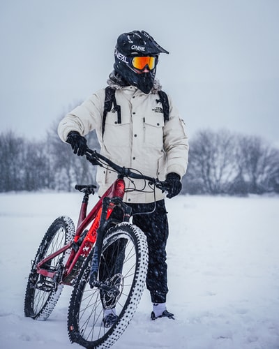 男人穿着白色夹克骑着红色和黑色山地车在冰雪覆盖的地面白天
